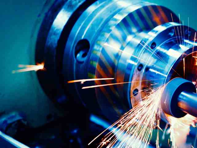 a machining tool spinning at high speed in a metal factory, causing sparks to fly from the metal work piece.