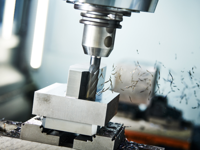 a CNC milling machine cutting into a metal piece, with small shavings flying out from the working material.