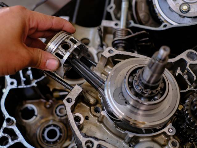 A hand working on repairing a piston inside of a motorcycle's engine block, revealing force torque sensors.